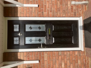 Black composite front door with decorative glazing in a red brick porch